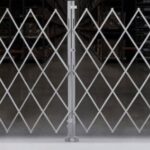 Closed diamond-pattern metal security gate in a warehouse, blocking access to storage racks.